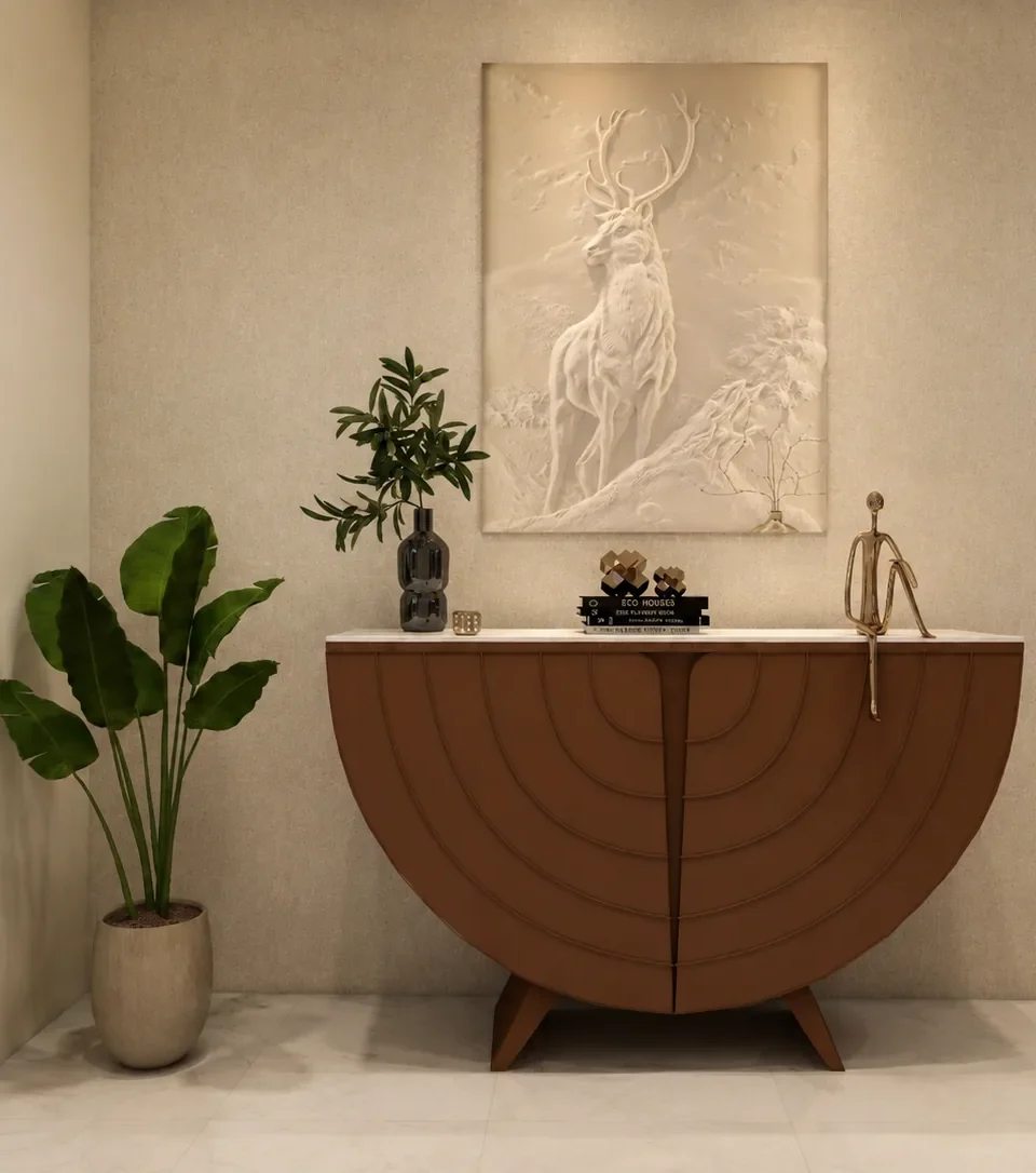 Foyer with a curved half-round tan console table on a splayed base, a sculpted white stag relief artwork, a potted plant and a brass figurine, on cream textured walls.